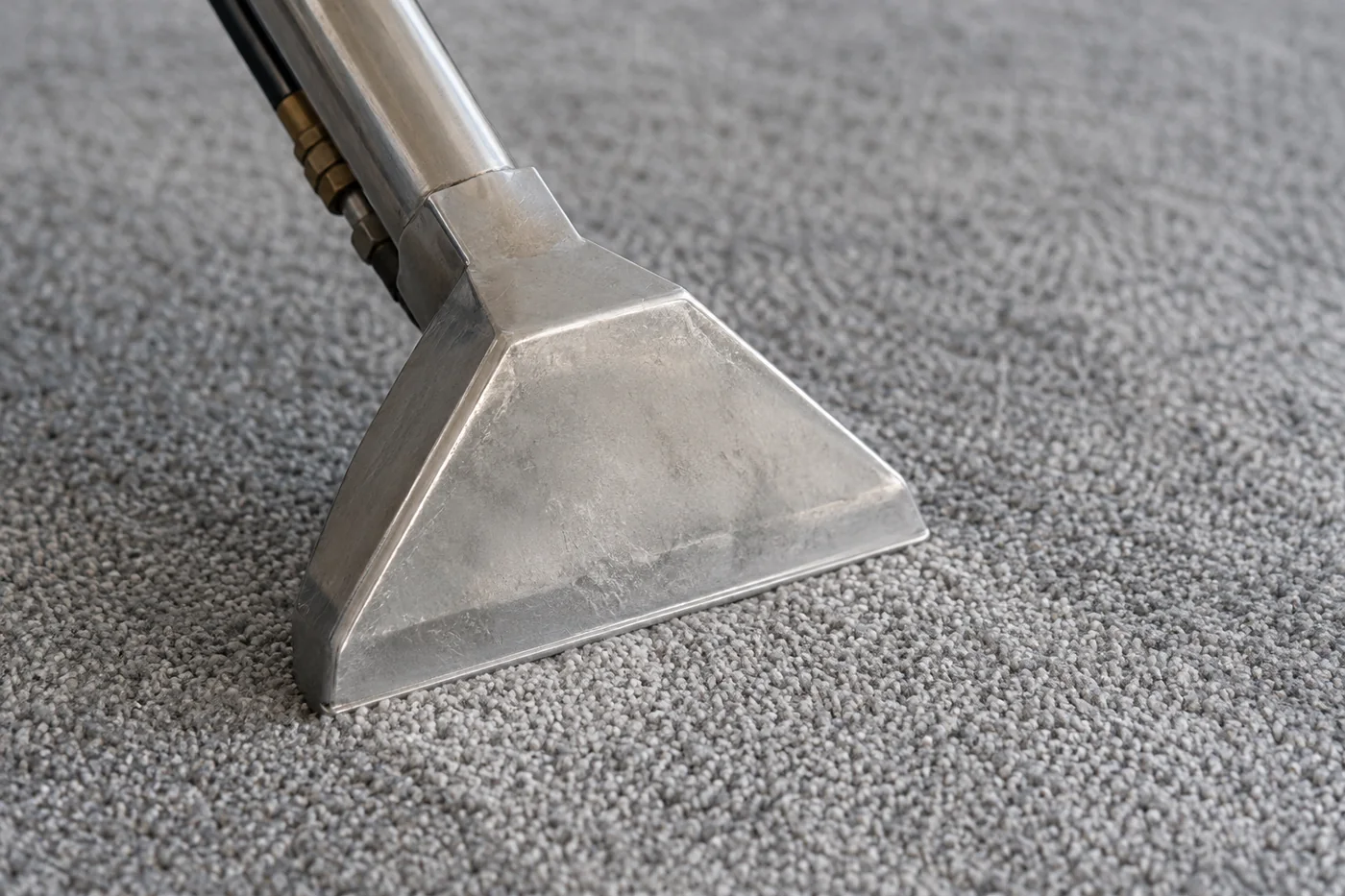 Metal carpet extraction wand head resting against neutral fitted carpet pile